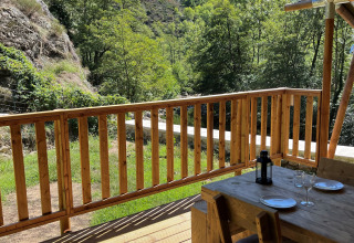 Vue d'une terrasse de tente safari avec mobilier en bois, collines verdoyantes et ciel bleu en France.