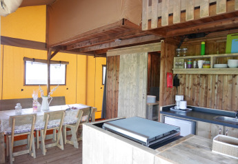 Interior de una tienda safari lodge con muebles de madera, mesa de comedor, cocina y baño propio.