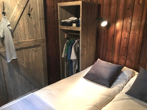 Camera da letto di una tenda safari a Camping l'Ardechois, con letto matrimoniale e armadio aperto in legno.