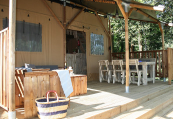 Terrasse extérieure d'un hébergement glamping avec salon en bois, table à manger et cadre forestier.