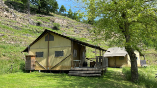 Tenda safari lodge con servizi igienici privati, immersa in una zona verde con colline e alberi.