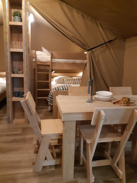 Interieur van een safaritent op Camping Le Bois de la Gachère in Frankrijk met eettafel en stapelbedden.