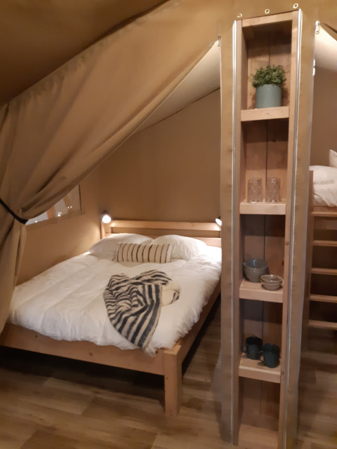 Schlafbereich in einem Safarizelt auf dem Campingplatz Le Bois de la Gachère in Frankreich mit Bett.