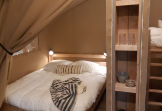 Soveområde i en safaritelte på Camping Le Bois de la Gachère i Frankrig med dobbeltseng og hylder.