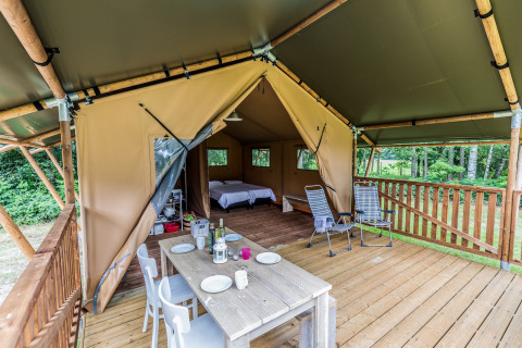 Safaritent met houten veranda, eettafel, loungestoelen en uitzicht op een bosrijke omgeving.