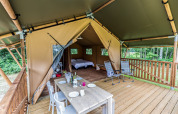 Tente safari avec terrasse en bois, table à manger extérieure, fauteuils et vue sur la forêt.