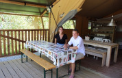 Due persone sedute a un tavolo all’interno di una tenda safari con arredi in legno e cucina sullo sfondo.