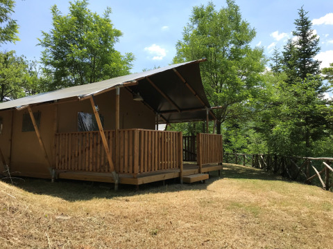 Safari tent met sanitaire voorzieningen op een grasveld, omgeven door groene bomen en natuur.