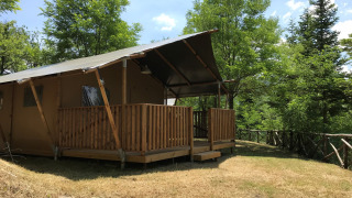 Tenda safari con servizi igienici su prato erboso, circondata da alberi verdi e natura rigogliosa.