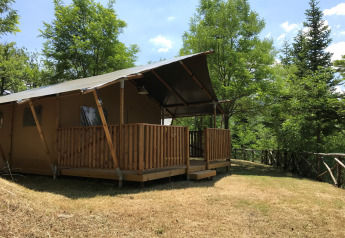 Tenda safari con servizi igienici su prato erboso, circondata da alberi verdi e natura rigogliosa.