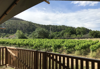 Vista desde la terraza de una tienda safari con valla de madera hacia campos verdes y colinas en Camping De l'Olivigne.