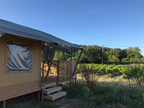 Tienda safari con veranda y sanitarios en Camping De l'Olivigne, vista a viñedos en Francia bajo cielo azul.