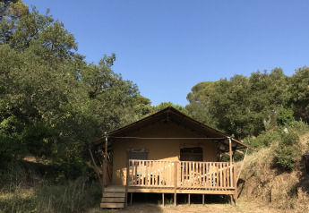 Safari-telt med sanitære faciliteter, omgivet af træer og natur under en klar blå himmel.