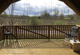 Vista dal terrazzo di una tenda safari con sedia, tavolo e barbecue al Camping Saint Amand in Francia.