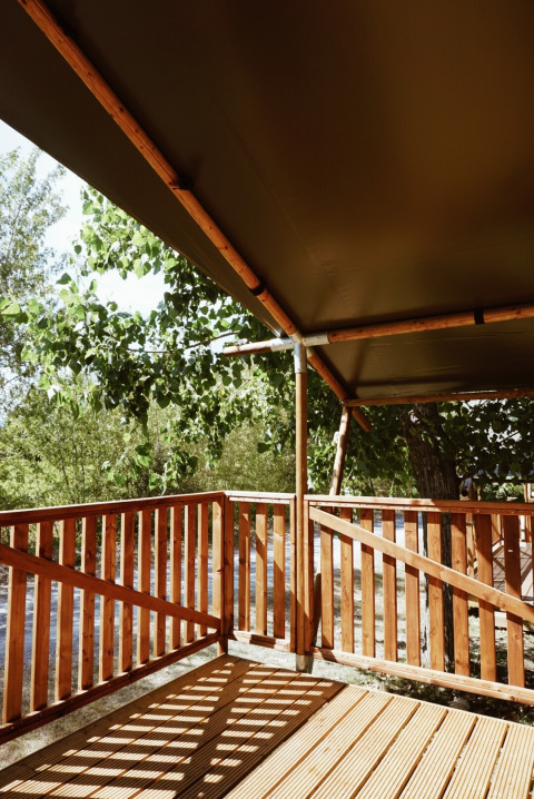 Holzterrasse mit Zaun und Überdachung an einem Safarizelt auf Camping Saint Amand in Frankreich, Naturkulisse.