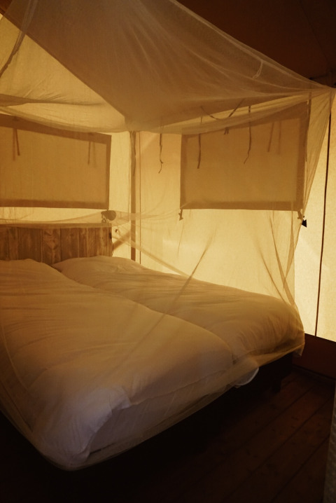 Innenansicht eines Safarizelts mit Moskitonetz und gemütlichen Betten auf Camping Saint Amand in Frankreich.