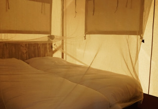Binnenaanzicht van een safaritent met muskietennet en comfortabele bedden op Camping Saint Amand in Frankrijk.