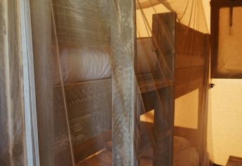 Bunk beds covered with mosquito netting inside a safari tent, softly illuminated in a cozy atmosphere.