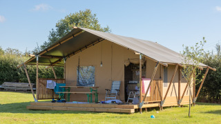 Safari tent with a wooden deck set on green grass, outdoor chairs and table under a clear blue sky