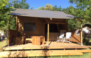 Tente safari Lodge avec terrasse en bois et chaises au camping Monti del Sole, Italie, entourée de verdure.