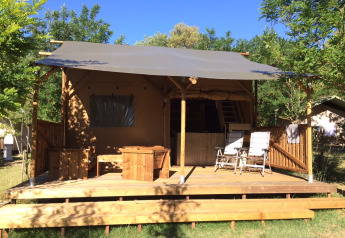 Safari Lodge-telt med træterrasse og stole på Camping Monti del Sole, Italien, omgivet af grønne træer.