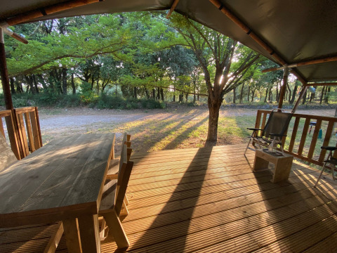 Houten veranda met tuinmeubilair bij een safaritent op Camping Monti del Sole in Italië, ochtendzon.