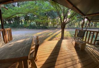 Houten veranda met tuinmeubilair bij een safaritent op Camping Monti del Sole in Italië, ochtendzon.