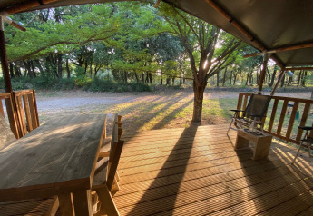 Wooden deck with outdoor furniture at a safari tent in Campsite Monti del Sole, Italy, morning sunlight.