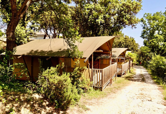 Safari tent with private sanitary facilities at Sierra campsite, surrounded by trees and greenery on a sunny day.
