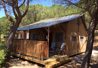 Safari-Zelt mit Veranda und Sanitäreinrichtungen im Wald, tagsüber bei blauem Himmel aufgenommen.