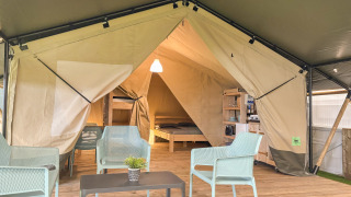 Vista interna di una tenda safari con sedute moderne, pavimento in legno e zona letto sullo sfondo.