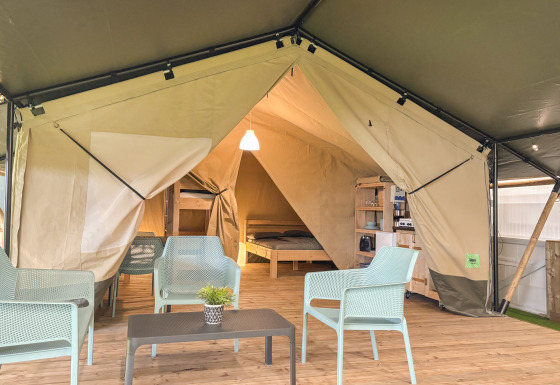 Vista interna di una tenda safari con sedute moderne, pavimento in legno e zona letto sullo sfondo.
