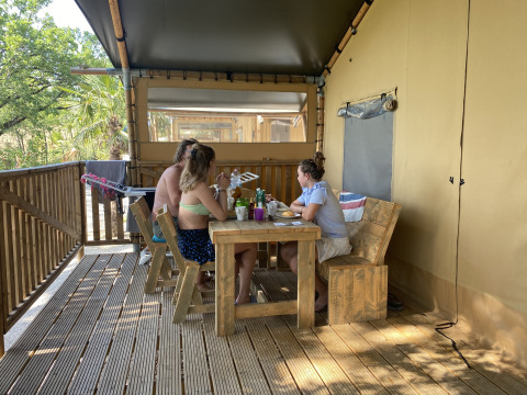 Mensen eten samen aan een houten tafel op de veranda van een safaritent op Camping Mar y Sierra in Italië.