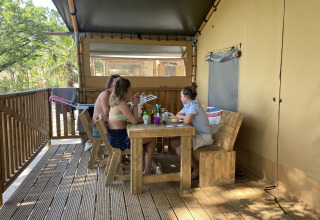 Folk sidder og spiser ved et træbord på terrassen i en safaritelte på Campingplads Mar y Sierra i Italien.