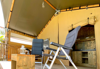 Coin salon sous tente safari au camping Mar y Sierra en Italie, avec fauteuils et petite table en bois.