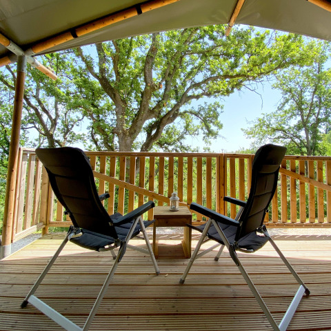 Due sedie su una veranda in legno sotto una tenda con vista sugli alberi al campeggio Mar y Sierra in Italia.