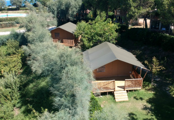 Buitenaanzicht van safaritenten met sanitaire voorzieningen omgeven door groen op Camping Paradiso in Italië.