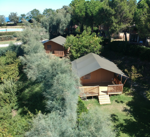 Vista exterior de tiendas safari con instalaciones sanitarias rodeadas de vegetación en Camping Paradiso, Italia.