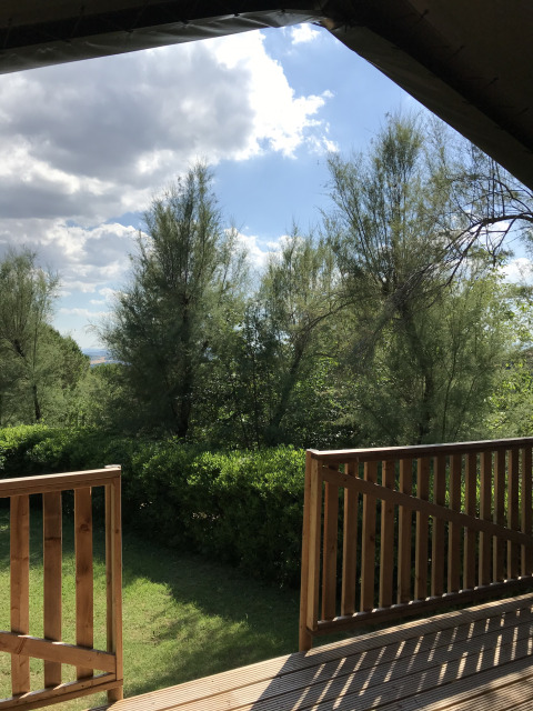 Udsigt fra en safaritelts terrasse på Camping Paradiso i Italien, omgivet af træer og sollys.