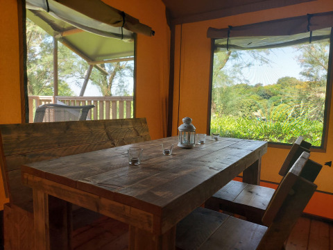 Houten eethoek in safaritent met zicht op de natuur in Camping Paradiso, Italië, met sanitair inbegrepen.