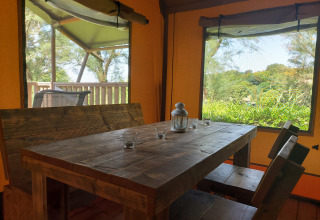 Wooden dining area inside safari tent with nature views at Camping Paradiso, Italy, with sanitary facilities.
