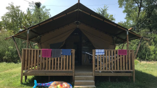 Safari-Zelt mit Holzveranda, bunten Handtüchern und aufblasbarem Schwimmring auf dem Rasen davor.