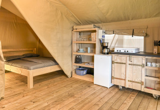 Vista interna di una tenda safari a Hvalpsund Familie Camping, Danimarca, con letto e cucina attrezzata.