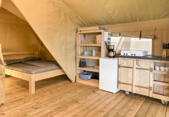 Vista interna di una tenda safari a Hvalpsund Familie Camping, Danimarca, con letto e cucina attrezzata.