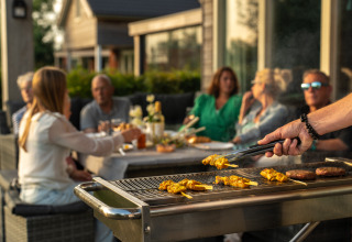 Barbecue en plein air dans un hébergement glamping, des invités savourent un repas et discutent ensemble.