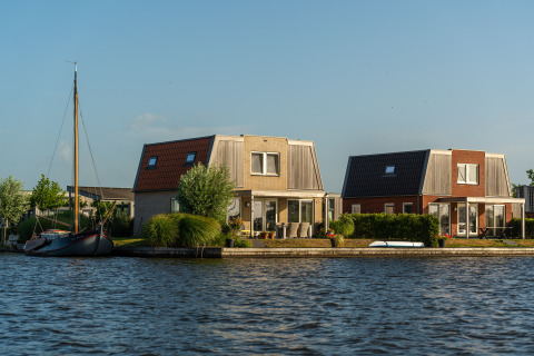 To moderne hytter ved søbredden med terrasse og båd, ideelt til glamping under en klar himmel.