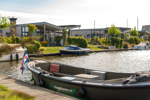 Barca ormeggiata su un canale davanti ad alloggi glamping moderni circondati dal verde.