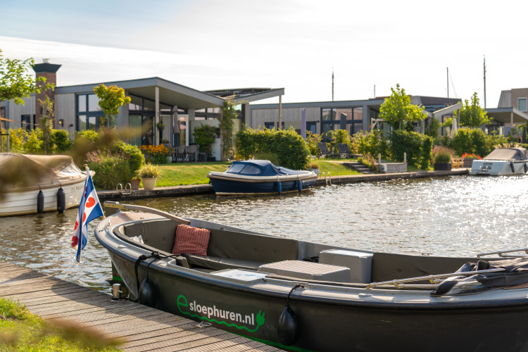Boot an einem Kanal vor modernen Glamping-Unterkünften, umgeben von gepflegten Gärten.