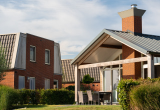 Moderne glampingboliger med røde murstensfacader og store vinduer, omgivet af grønne planter og himmel.