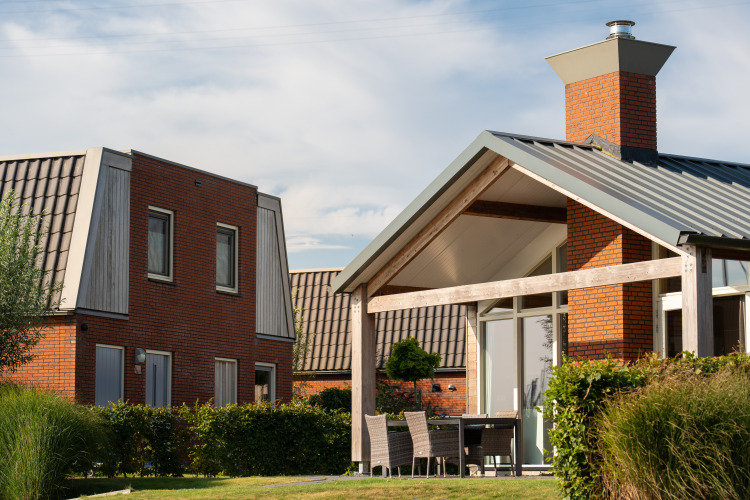 Moderne glampingaccommodatie met bakstenen muren, grote ramen, buitenterras en groene tuin.